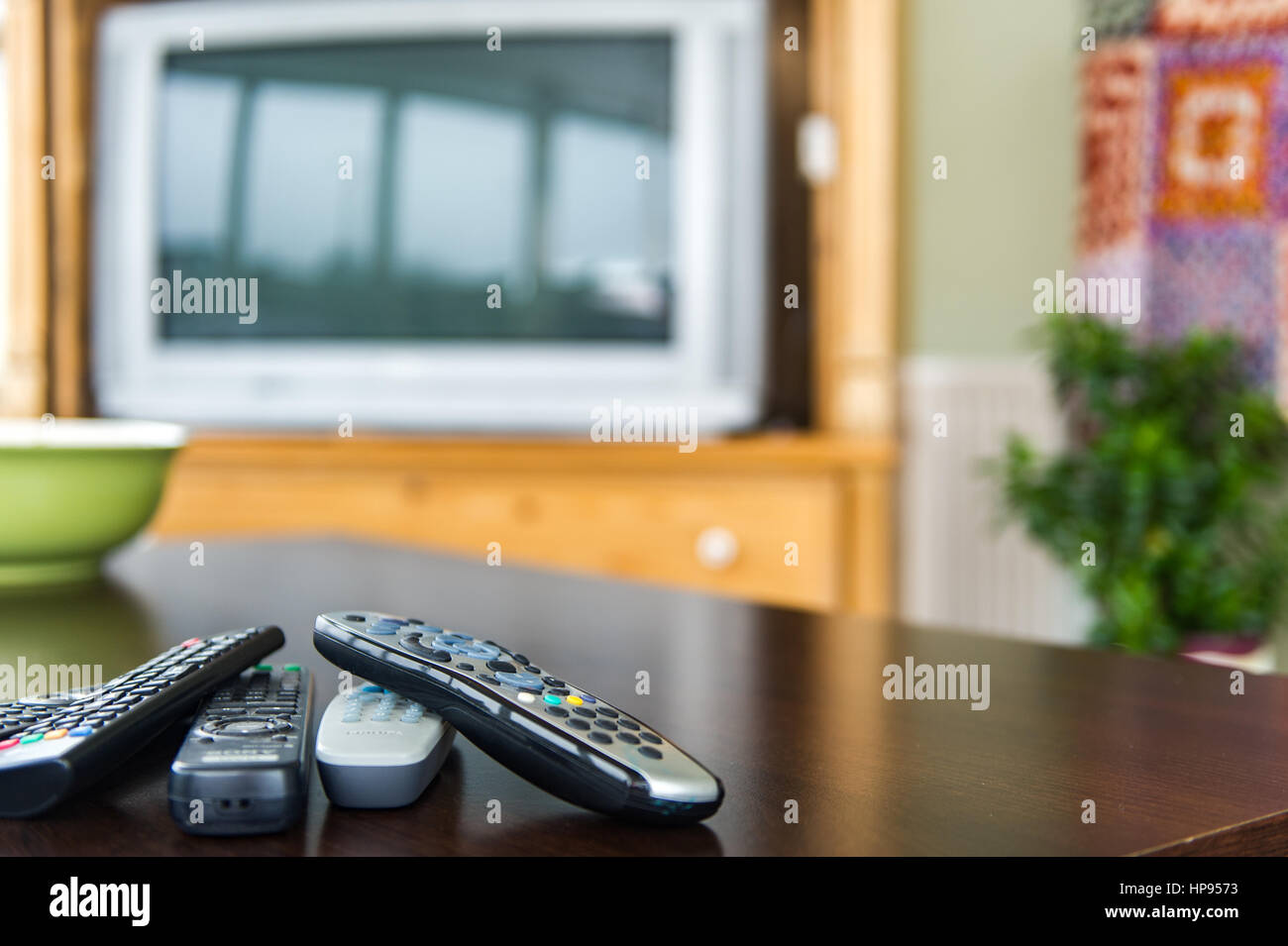 Fernbedienungen auf einem Couchtisch vor einem Fernseher als ein Technologiekonzept. Stockfoto