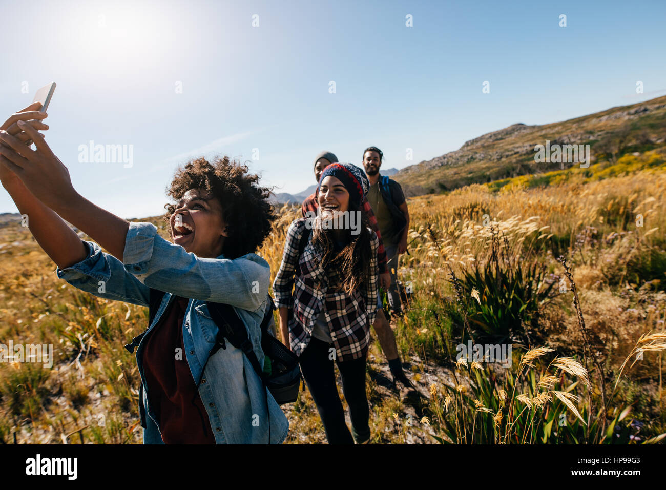 Glückliche junge Frau Fotos von Freunden beim Wandern. Gruppe von Freunden auf Land zu Fuß nehmen Selfie. Stockfoto