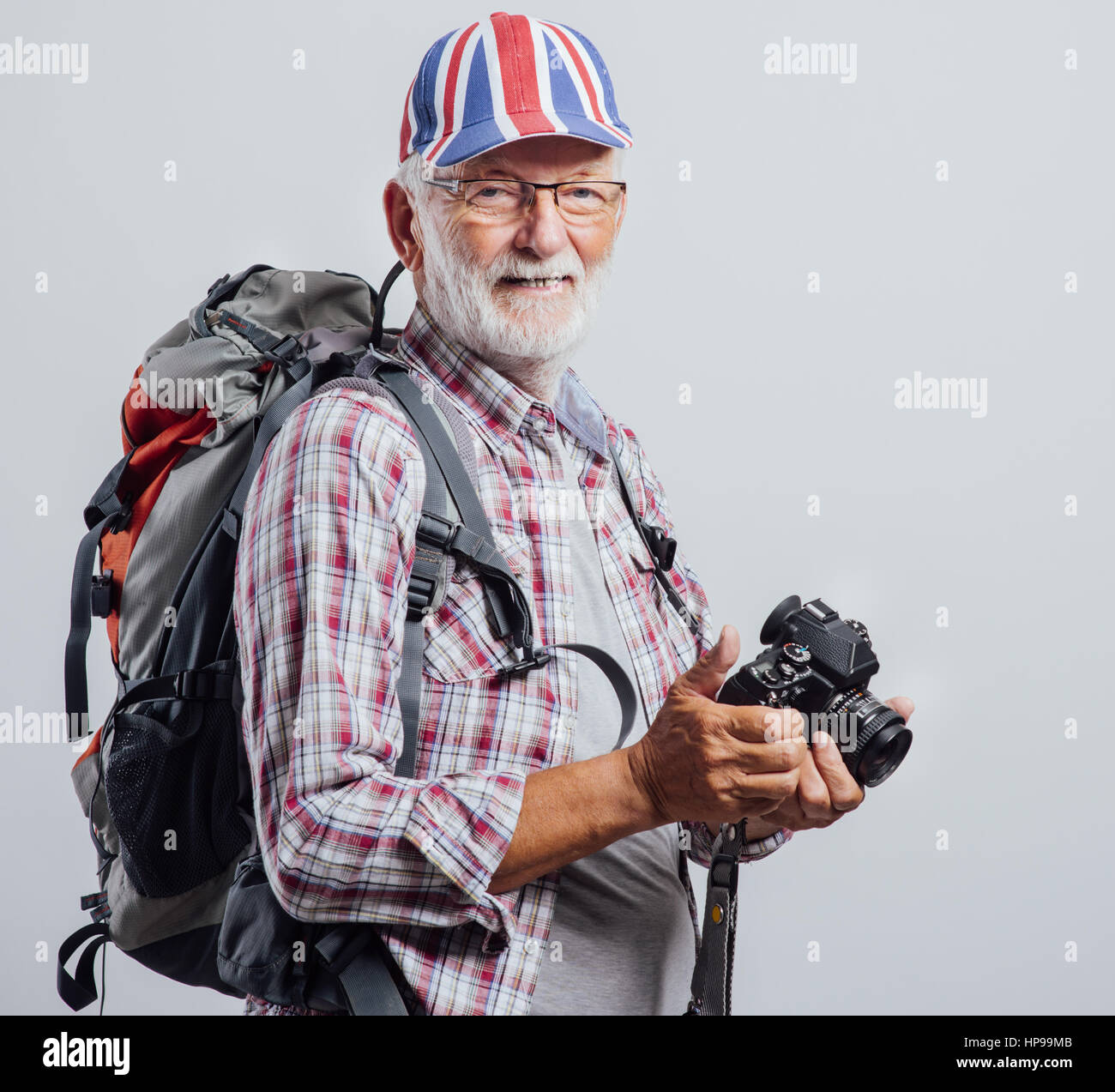 Senior-Explorer mit Rucksack posieren und halten Sie eine digitale Kamera, trägt er eine britische Flagge-Kappe Stockfoto