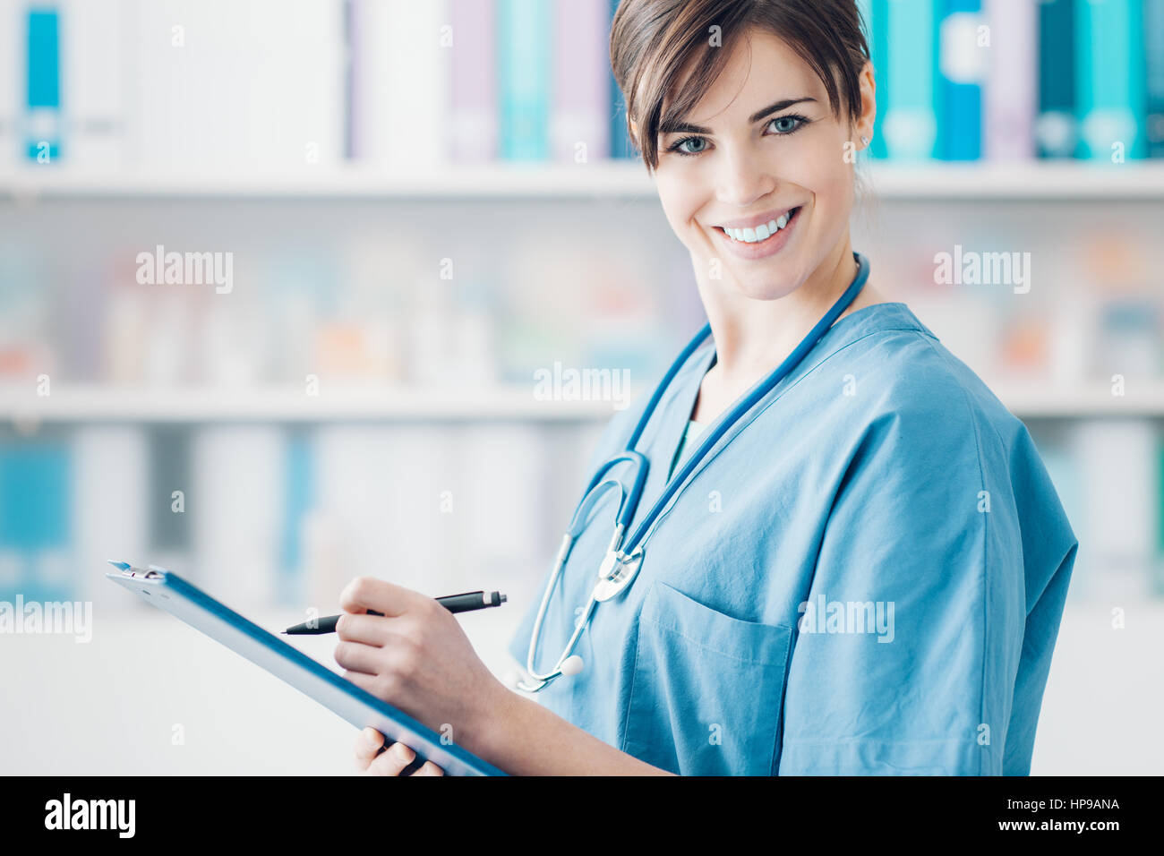 Lächelnde junge Ärztin, die einen medizinischen Bericht auf einem Klemmbrett, medizinisches Fachpersonal zu schreiben Stockfoto