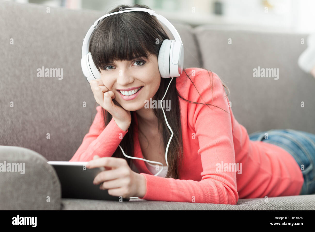 Lächelnde junge Frau zu Hause auf der Couch entspannen, trägt Kopfhörer, sie mit einem digital-Tablette und einen Film online Stockfoto