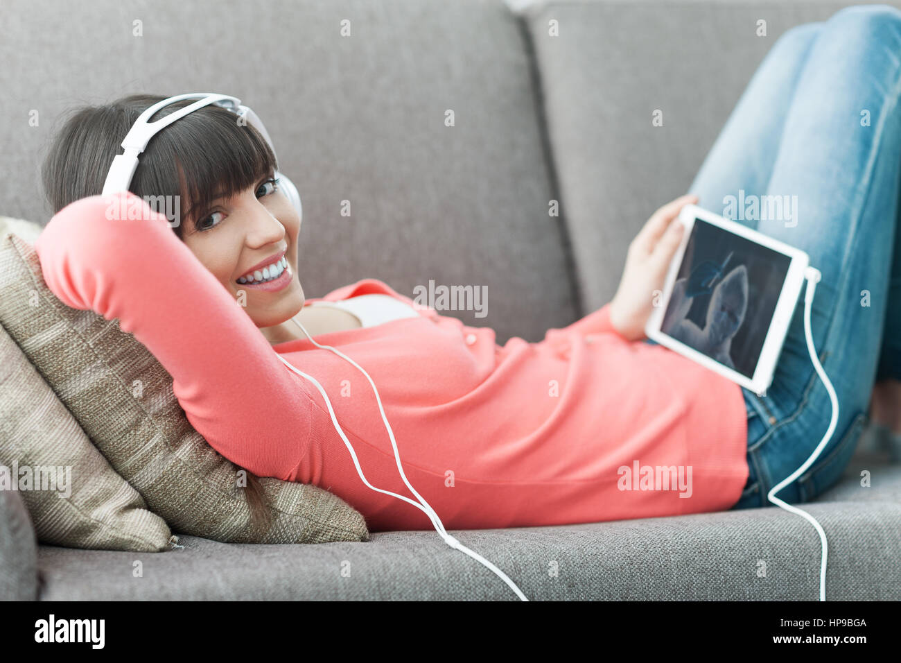 Lächelnde junge Frau zu Hause auf der Couch entspannen, trägt Kopfhörer, sie mit einem digital-Tablette und ein Video online ansehen Stockfoto