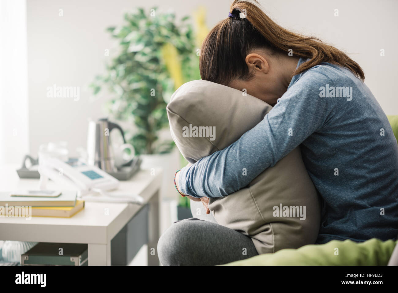 Unglücklich einsam depressiv Frau zu Hause, sie sitzt auf der Couch und versteckt ihr Gesicht auf einem Kissen, Depression-Konzept Stockfoto