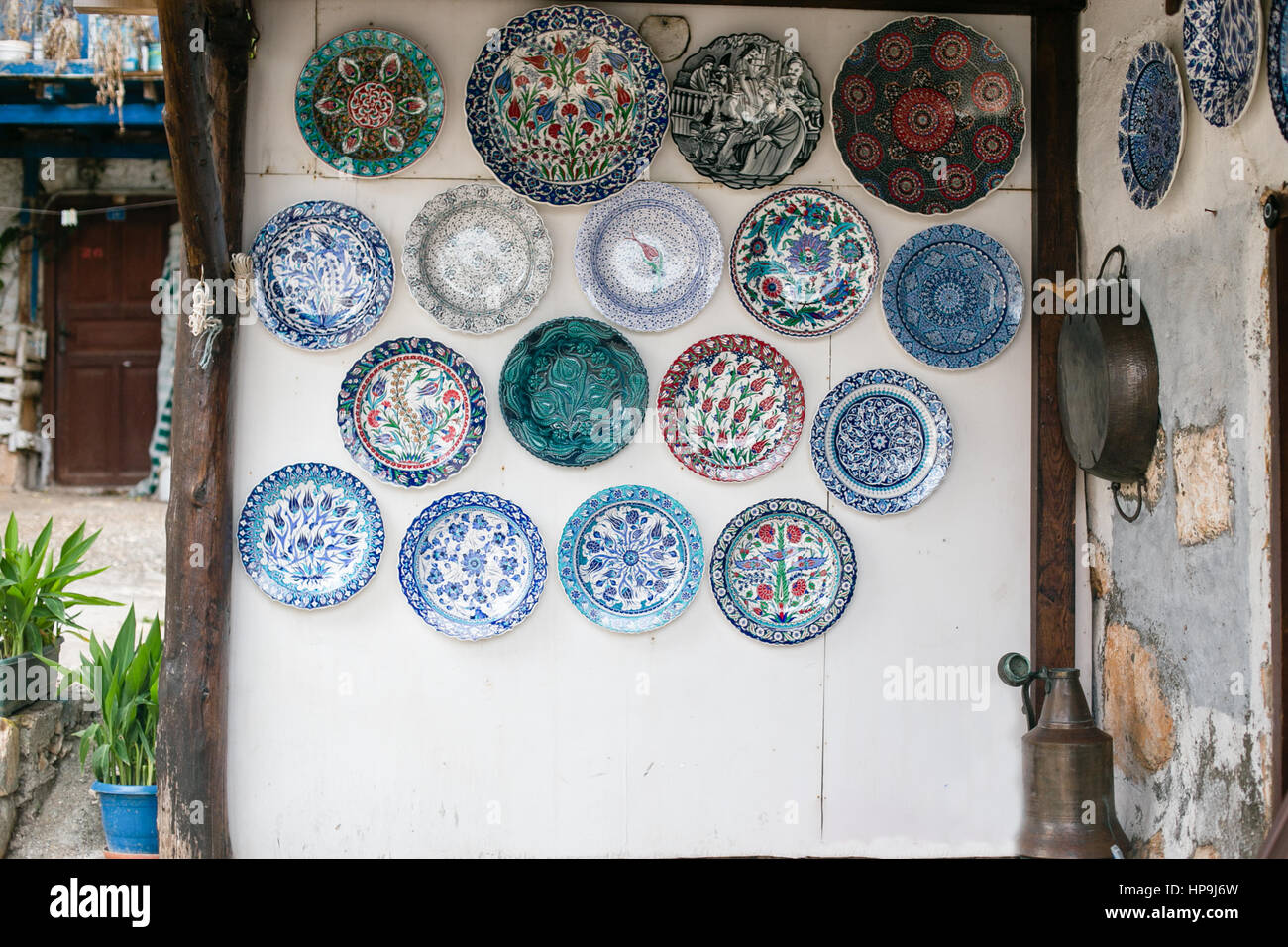 Weißer Wand dekoriert mit vielen keramischen Platten in blau und türkis-Tönen mit Pflanzen in Töpfen auf der linken Seite und Eisen Tablett hangin an Wand auf der rechten Seite Stockfoto