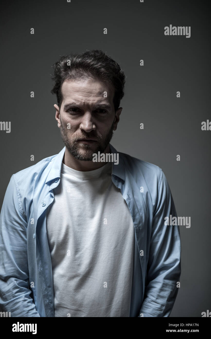 Schlechte Laune. Junge männliche Person drücken Lippen während Ausdruck Negativität tragen blaues Hemd über weißes t-Shirt mit Blick direkt in die Kamera Stockfoto