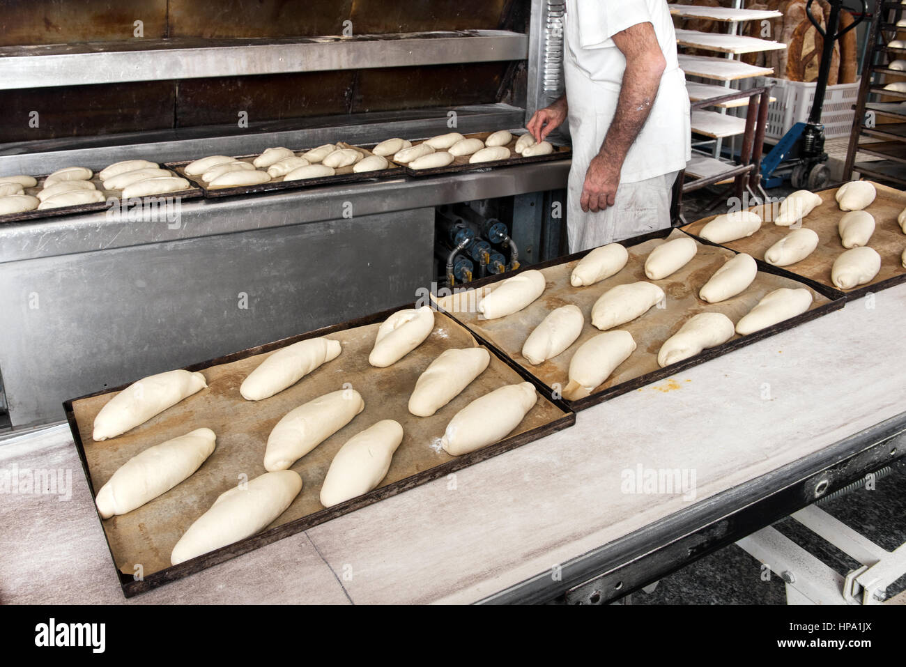 Inkognito männlichen Bäcker in weißem Hemd, die Herstellung von Brot, einige Töpfe mit Teiglinge kochbereit lange Brote auf den Tischen der Bäckerei Stockfoto