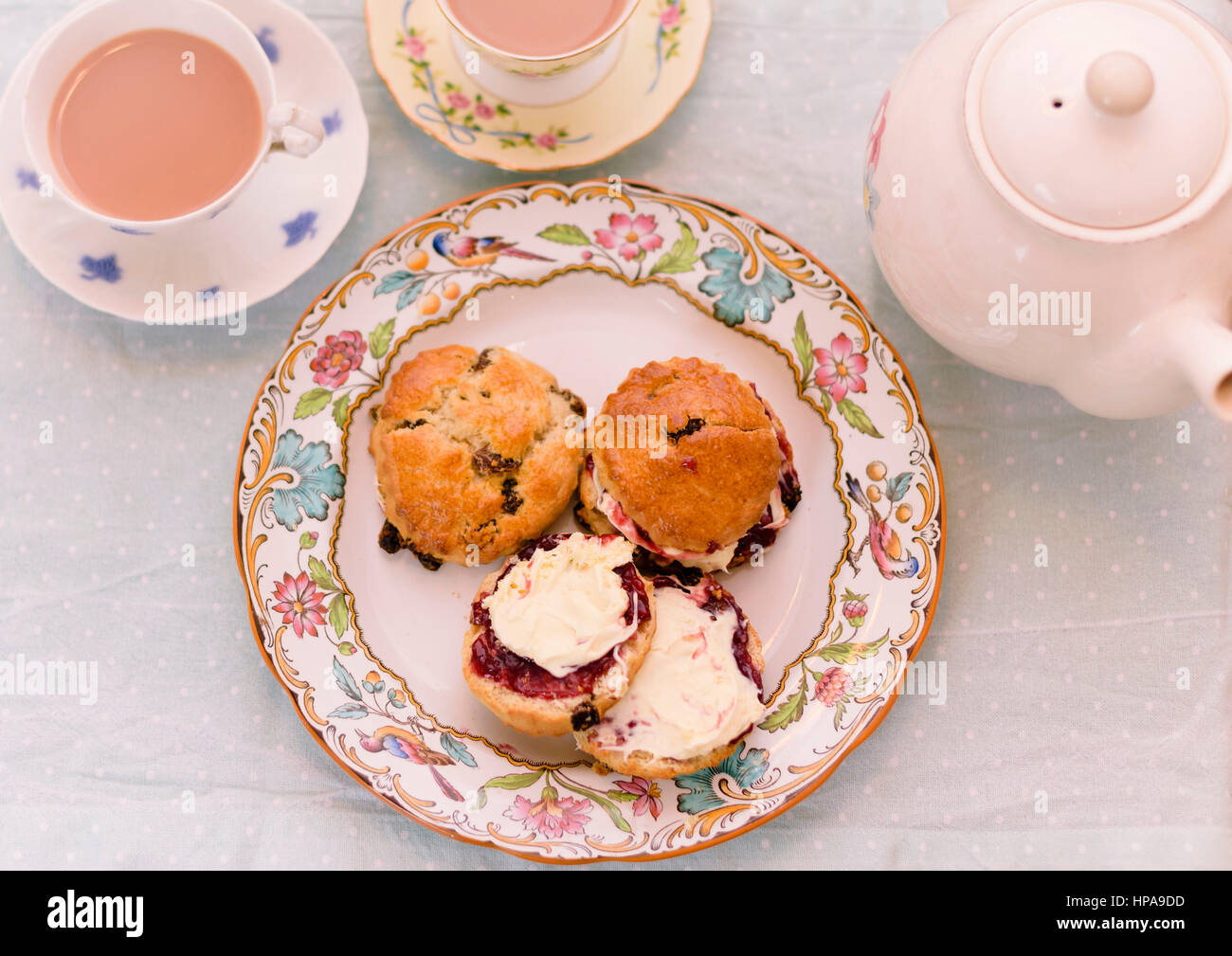 Cream Tea. Tassen Tee und Scones mit Marmelade und Clotted Cream, begleitet von einem Weidenkorb gefüllt mit Stoff Stockfoto