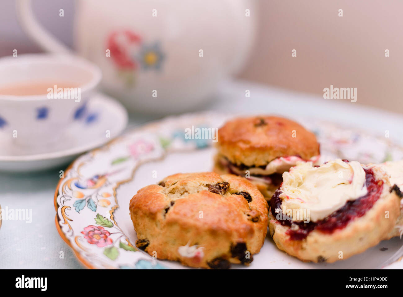 Cream Tea. Tassen Tee und Scones mit Marmelade und Clotted Cream, begleitet von einem Weidenkorb gefüllt mit Stoff Stockfoto