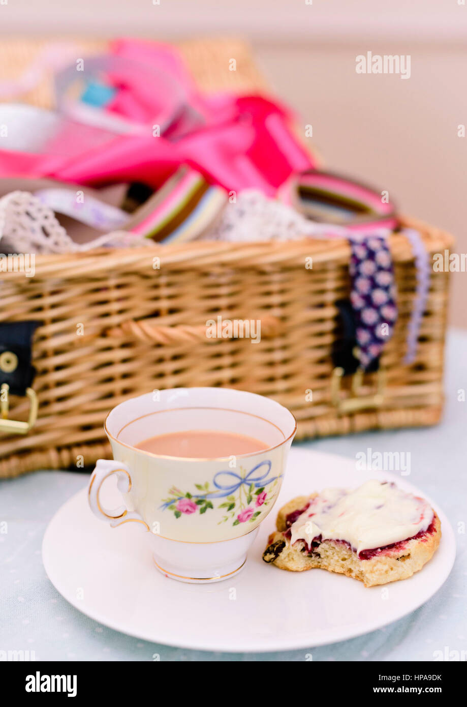 Cream Tea. Tassen Tee und Scones mit Marmelade und Clotted Cream, begleitet von einem Weidenkorb gefüllt mit Stoff Stockfoto