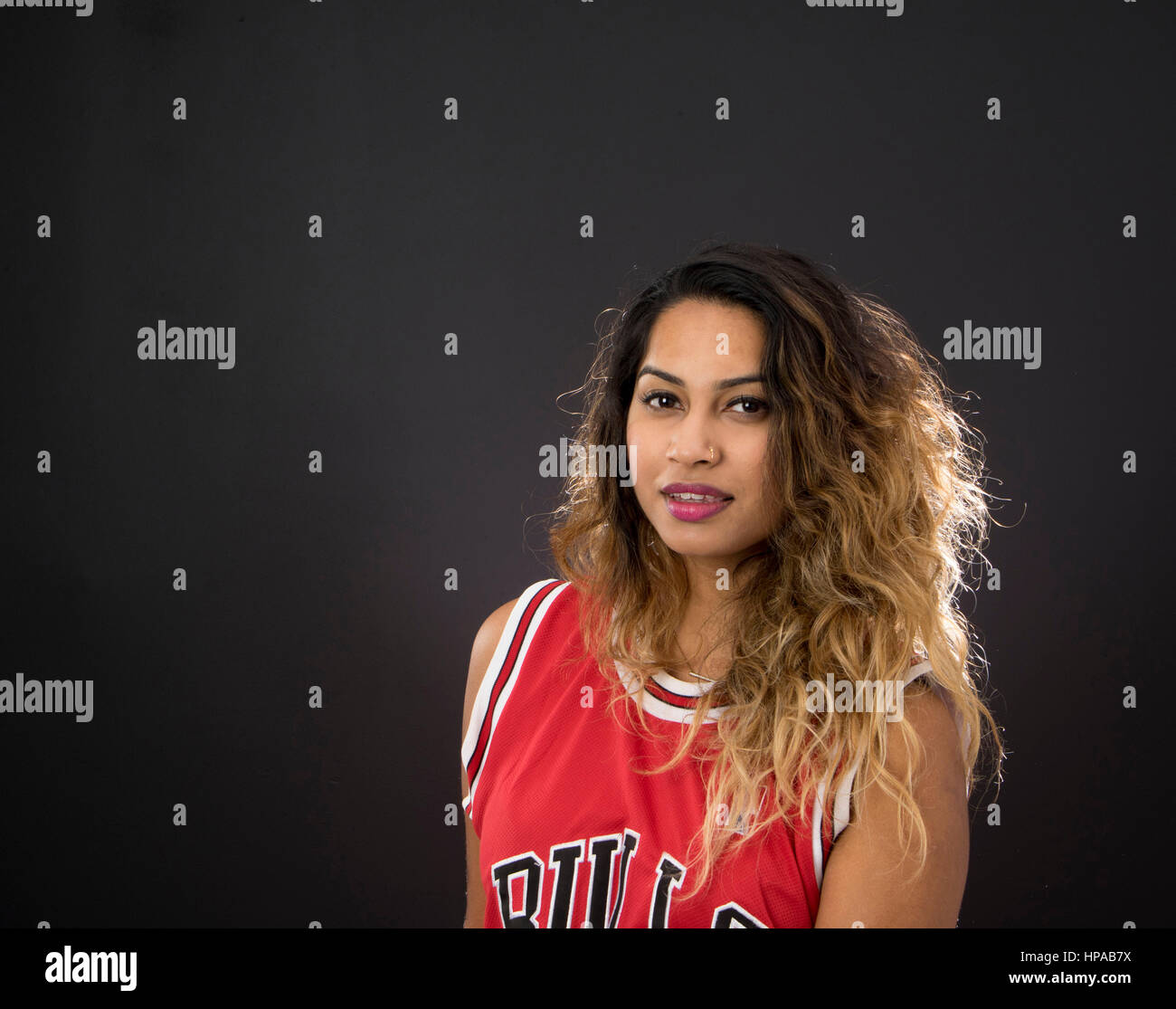 Junge indische Frau mit langem Haar, lächelnd und trug ein ärmelloses roten Sport Jersey, schwarzer Hintergrund Stockfoto