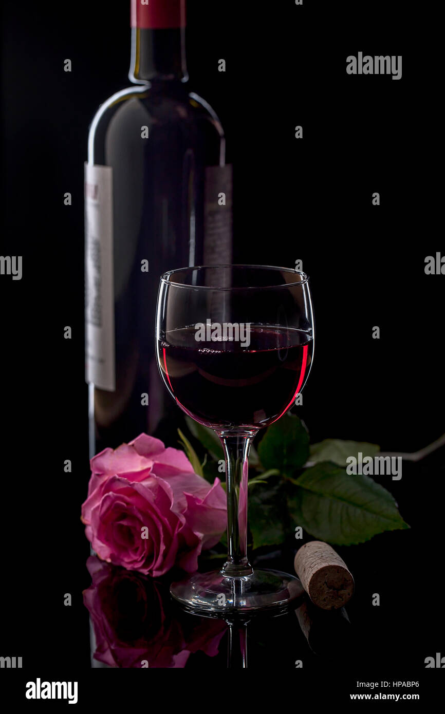 Eine Nahaufnahme der Stillleben mit Rotwein, eine Flasche und Korken und eine rosa Rose. Stockfoto