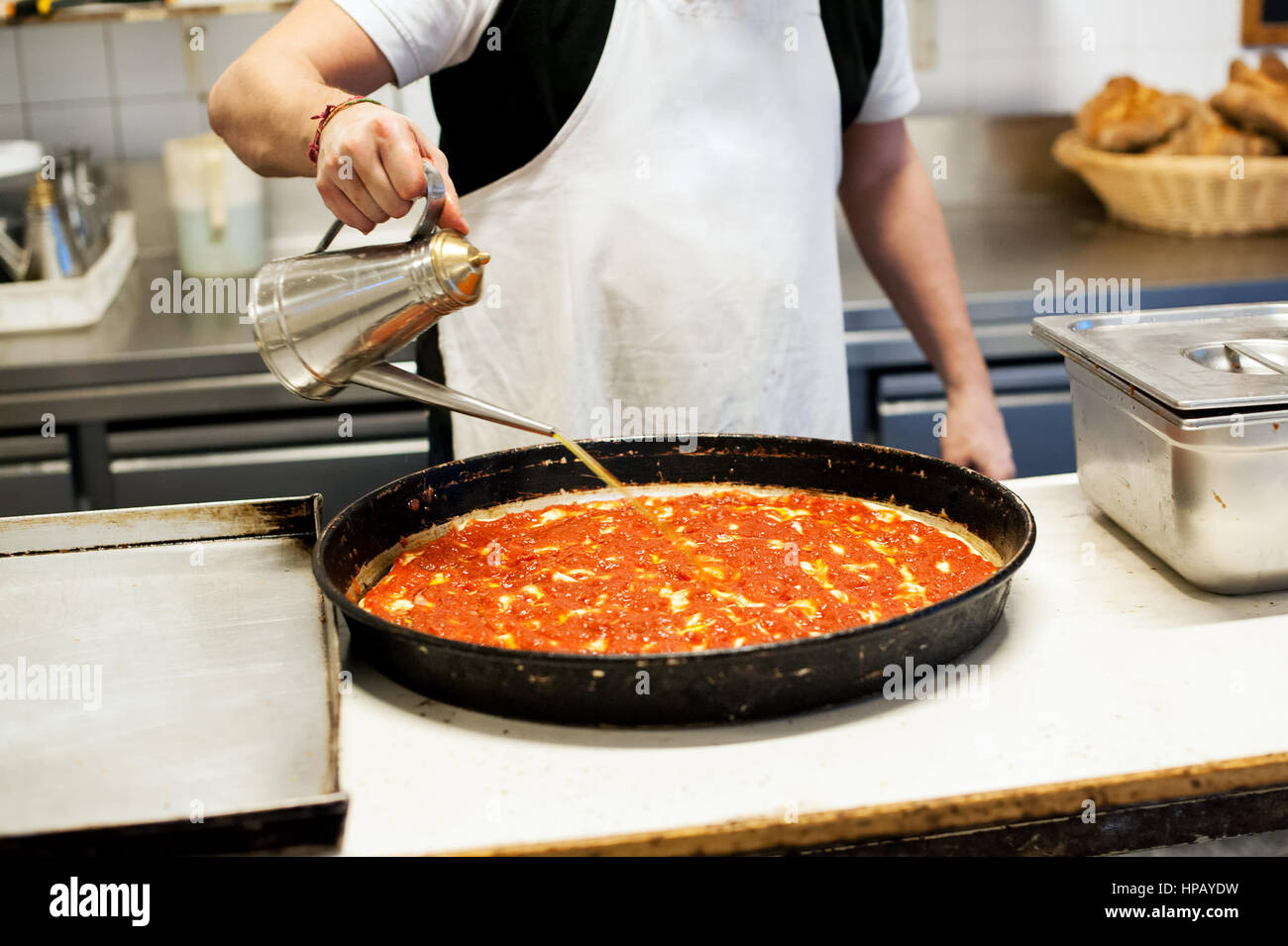 Italienisches Restaurant Koch Öl aus alten Kessel auf Pizza vor dem Backen in tiefen Pfanne gießen Stockfoto