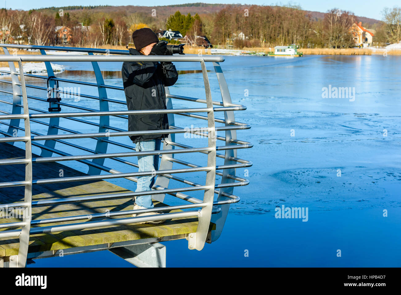 Junge Fotografen Aufnahme auf Brücke mit eisigem Wasser stehend nach unten unten. Kalten, aber sonnigen Tag im Frühjahr oder im Winter. Landschaft in backg Stockfoto