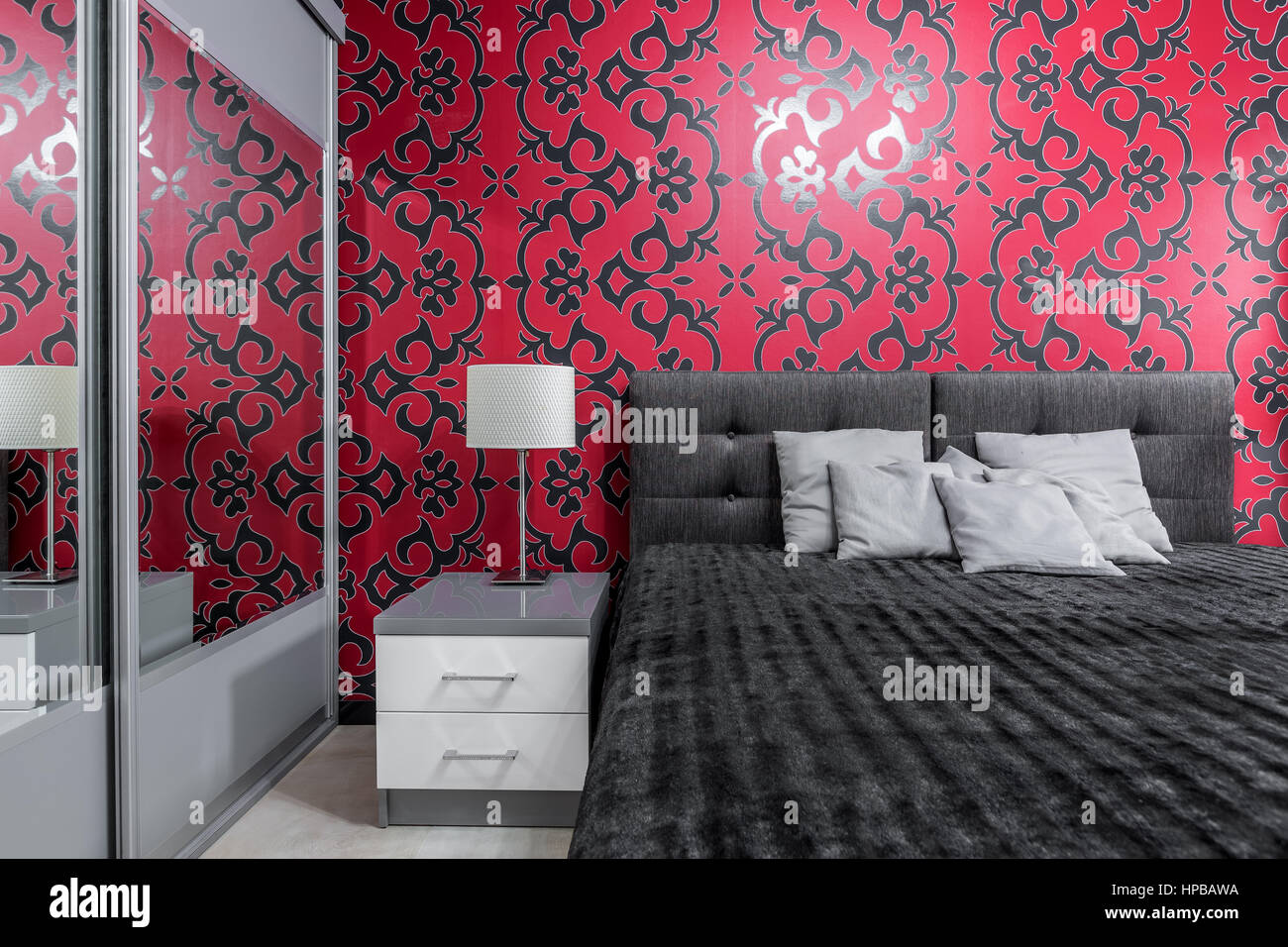 Gemütliches Schlafzimmer mit großem Bett und gemusterte schwarze und rote Wand Stockfoto