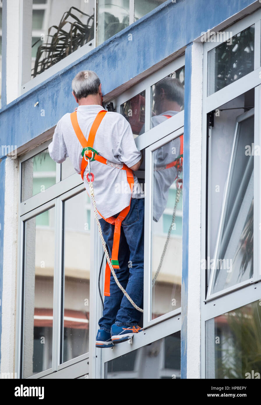 Mann mit Elektrowerkzeug balancieren prekär auf Fenstersims. Stockfoto