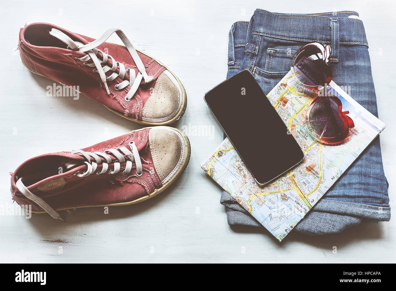 Kleidung & Zubehör: Hipster Turnschuhe, Jeans, kariertes Hemd, Cowboy Gürtel, Telefon mit Kopfhörern auf hölzernen Hintergrund. Reisen-Konzept Stockfoto