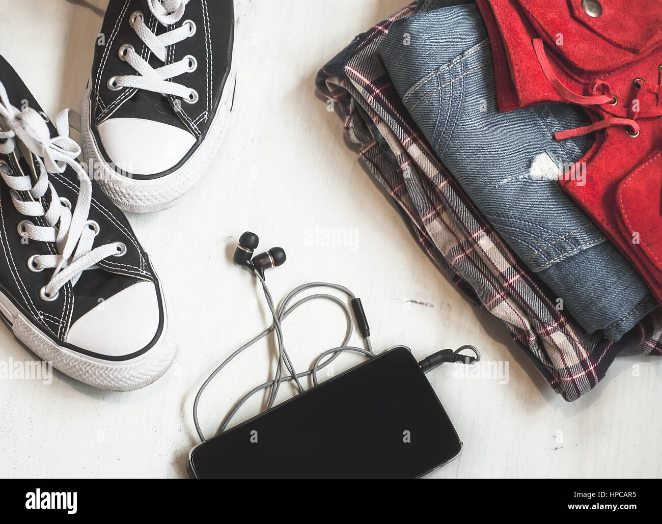 Kleidung & Zubehör: Hipster Turnschuhe, Jeans, kariertes Hemd, Cowboy Gürtel, Telefon mit Kopfhörern auf hölzernen Hintergrund. Reisen-Konzept Stockfoto