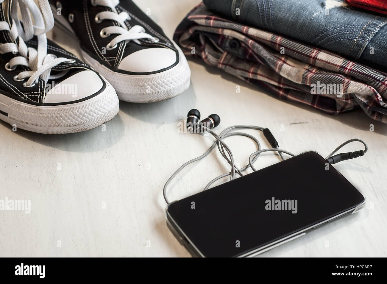 Kleidung & Zubehör: Hipster Turnschuhe, Jeans, kariertes Hemd, Cowboy Gürtel, Telefon mit Kopfhörern auf hölzernen Hintergrund. Reisen-Konzept Stockfoto