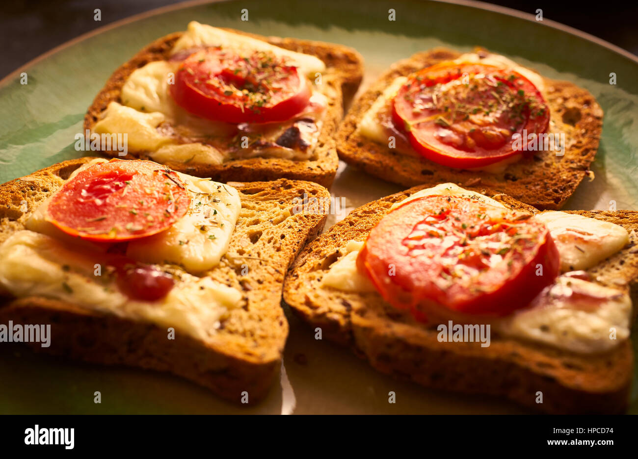 Geschmolzene Käse auf Toast mit in Scheiben geschnittenen Tomaten und Kräutern Stockfoto