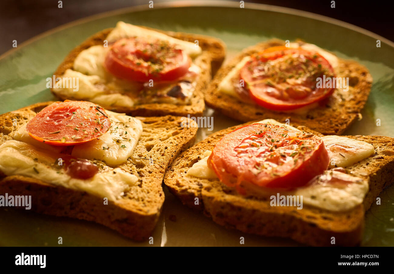 Geschmolzene Käse auf Toast mit in Scheiben geschnittenen Tomaten und Kräutern Stockfoto