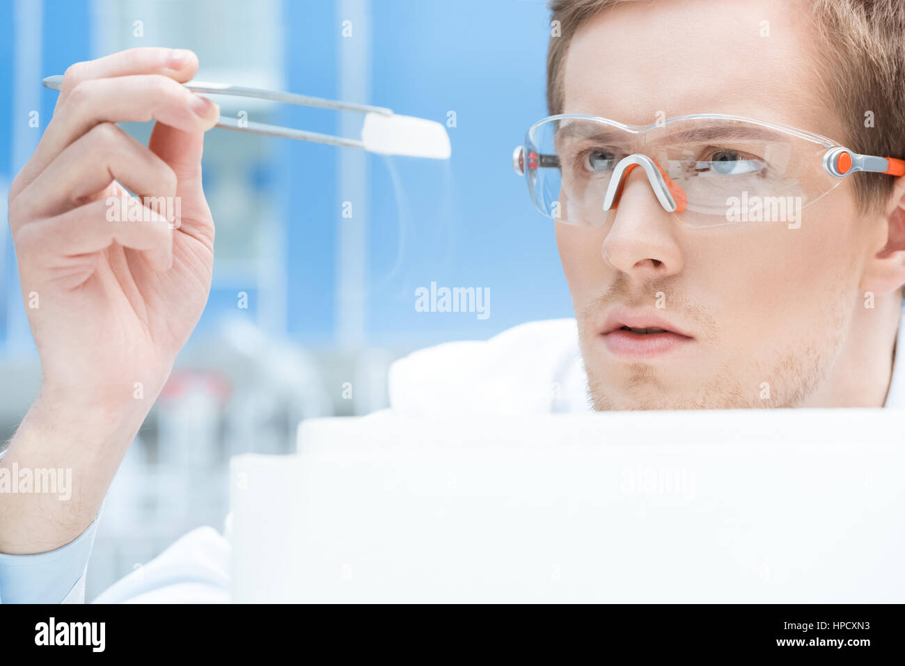 konzentrierte Wissenschaftler in Schutzbrille und Handschuhe Blick auf chemische Probe Stockfoto
