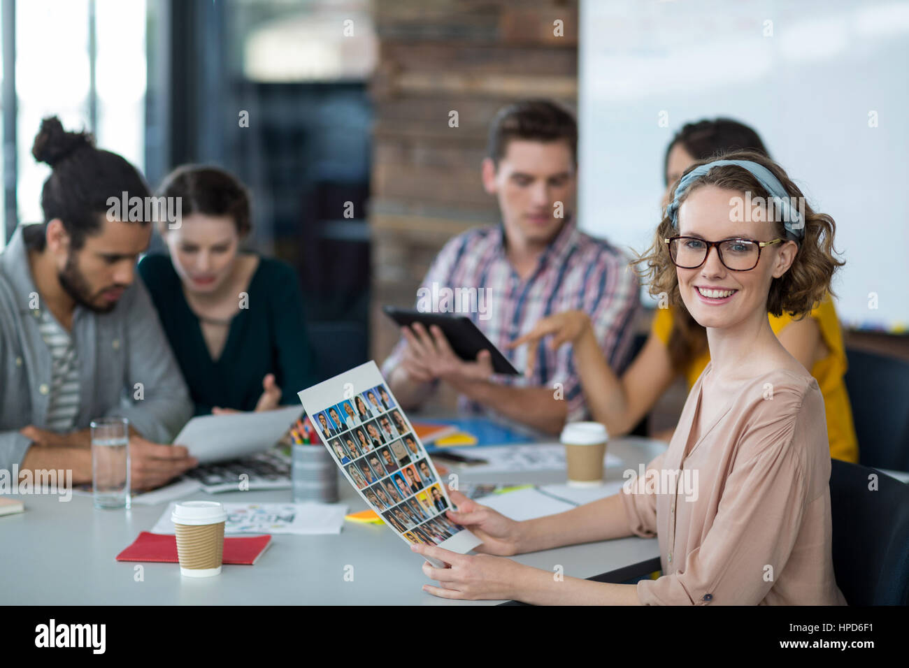 Porträt des Lächelns Grafik Designer Holding Fotos im Büro beim Kollegen diskutieren im Hintergrund Stockfoto