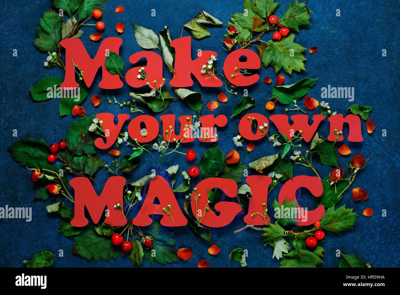 Machen Sie Ihre eigene Magie Schriftzug mit grünen Blättern und roten Rosenblüten. Buchstaben bestehen aus pastellfarbenen Papier. Stockfoto