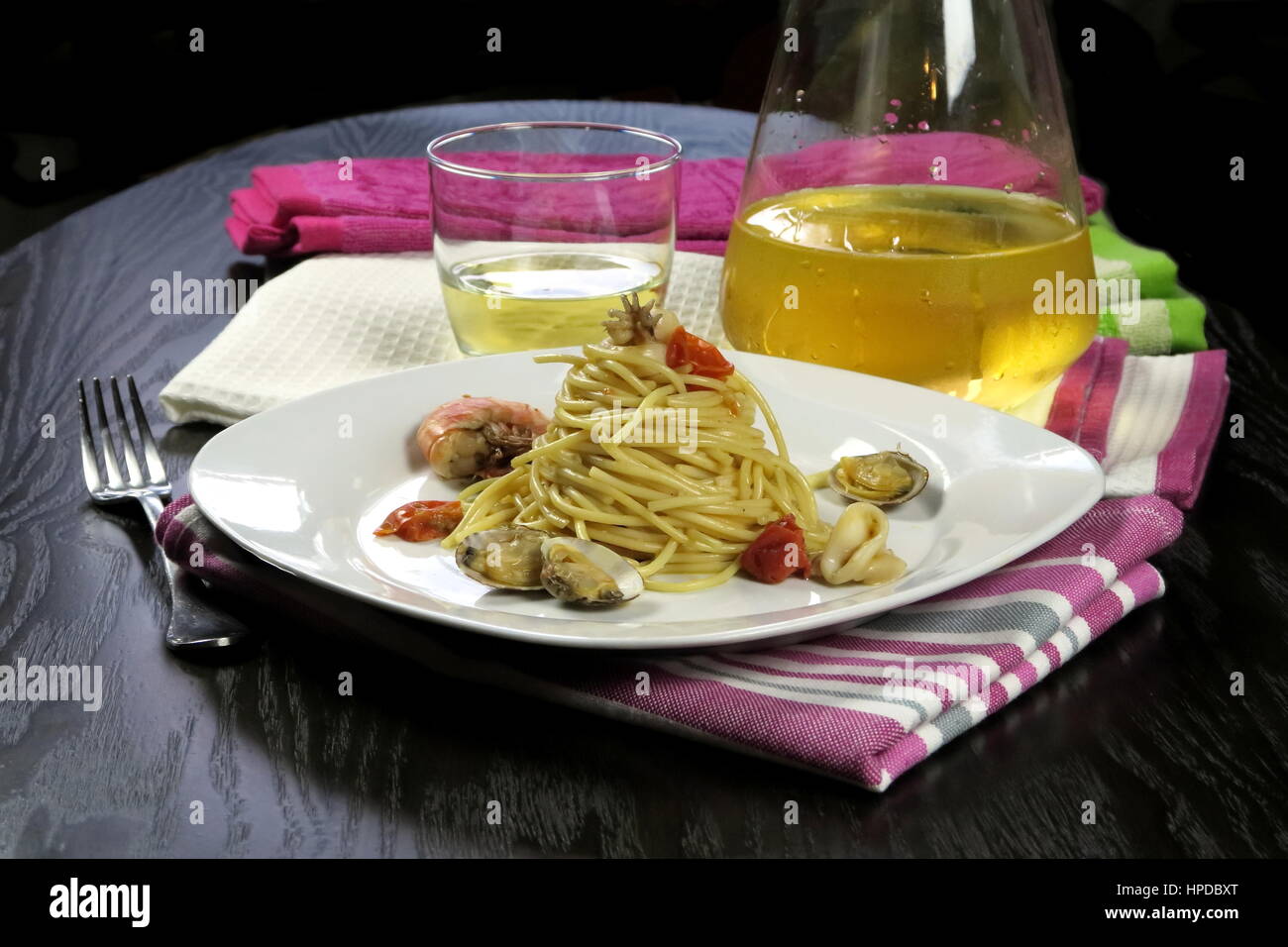 Pasta mit Meeresfrüchten in weißen Schale auf bunte Küchentücher und kühlen Weißwein (Glas und Karaffe) im Hintergrund. Italienische Spaghetti allo Scoglio Rezept Stockfoto