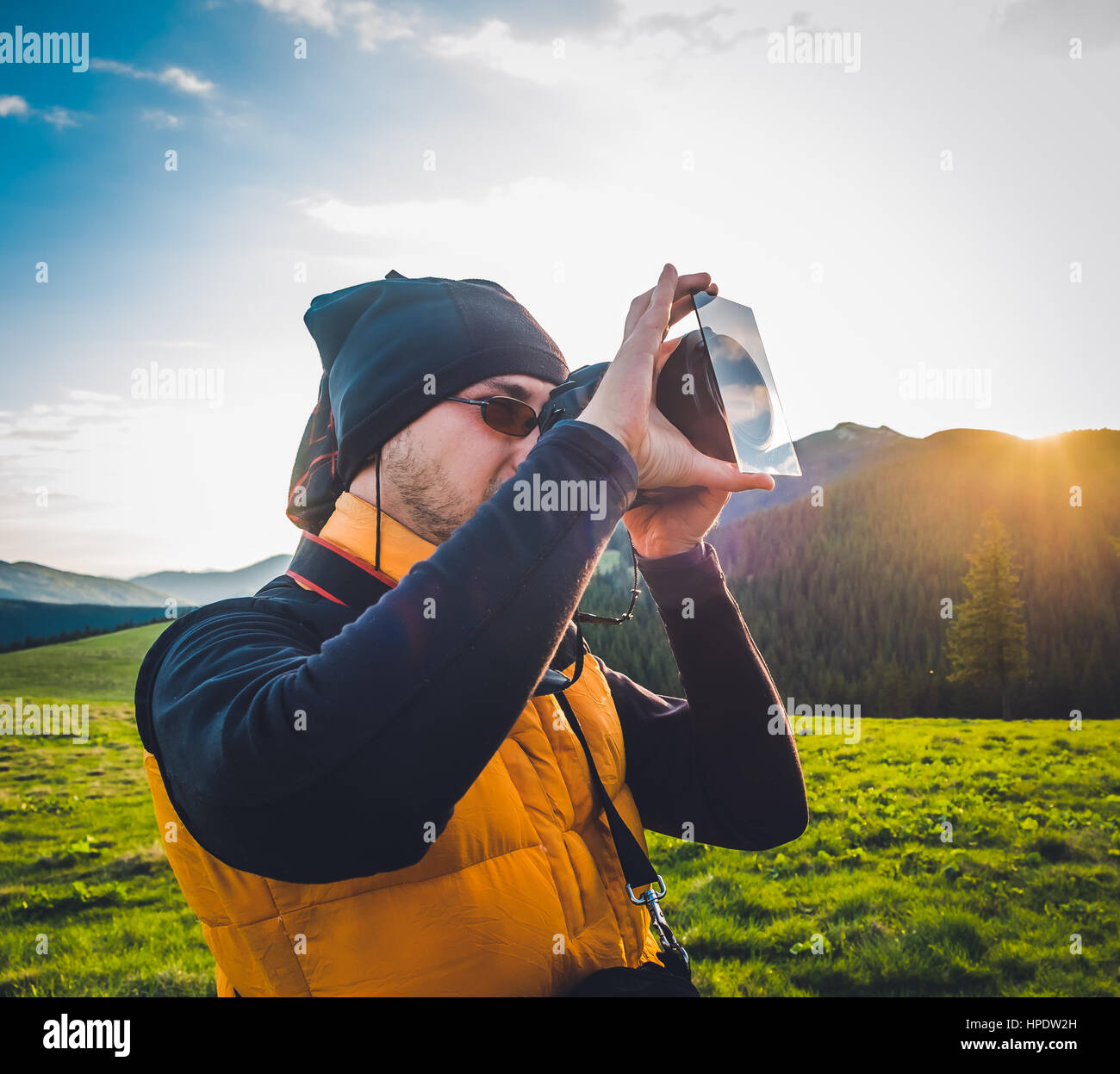 Natur-Fotograf-Tourist mit Kamera fotografieren in den Bergen. Traumhafte Sonnenuntergang Landschaft, Frühlingsgrün Wiese und Mountain Top in der staatlich Stockfoto