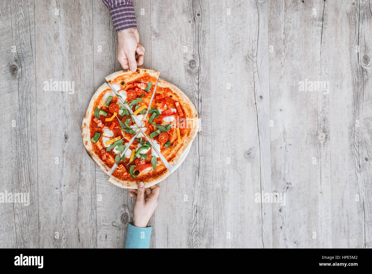 Freunde teilen eine leckere Pizza auf einem rustikalen Tisch, halten sie ein Slice, Ansicht von oben Stockfoto