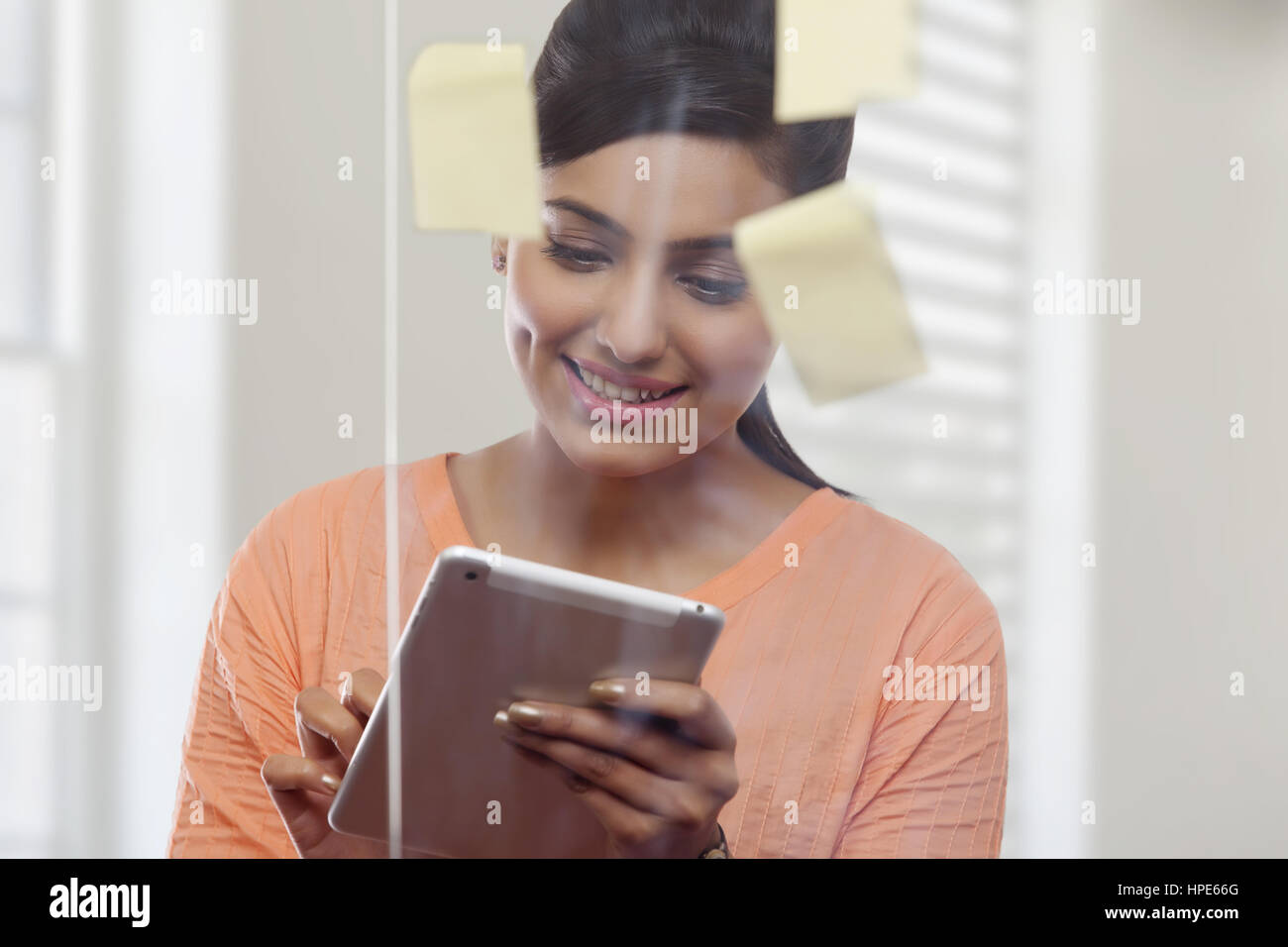 Frau hinter Glasscheibe mit Klebstoff Noten mit digital-Tablette in office Stockfoto