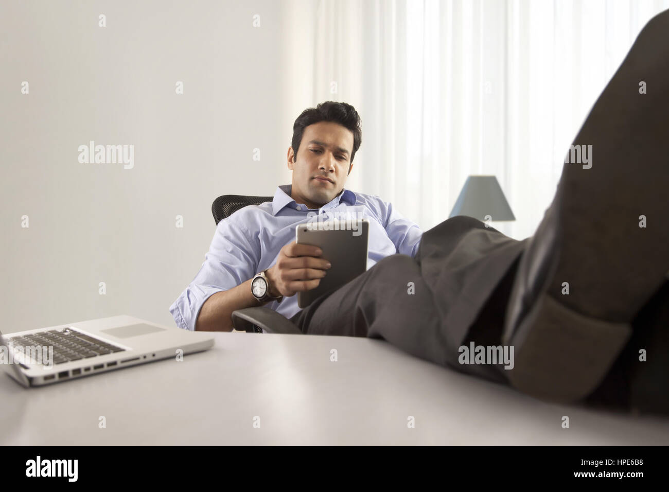 Porträt eines Geschäftsmannes am Schreibtisch mit seinen Füßen bis und mit digital-Tablette Stockfoto