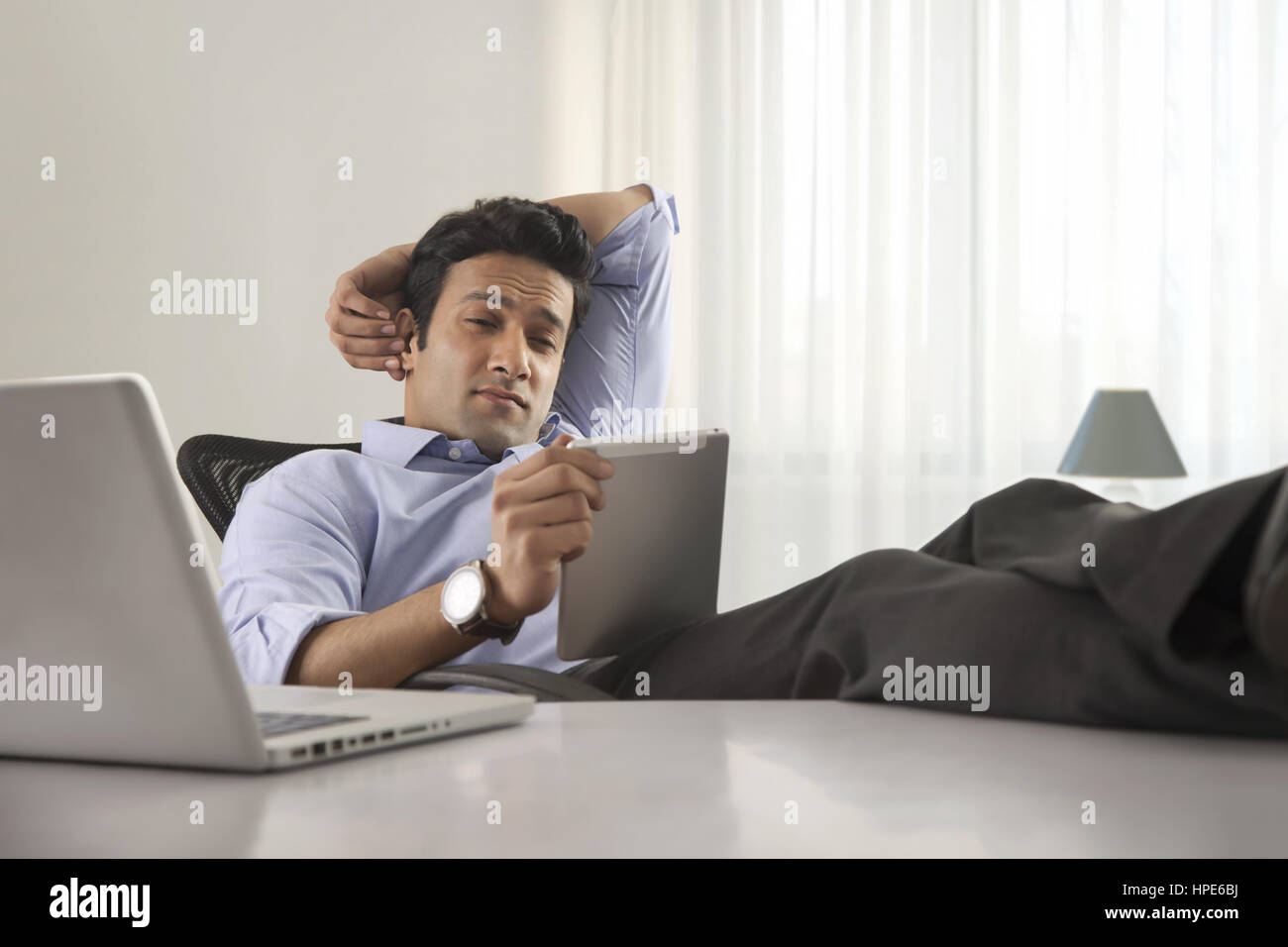 Porträt eines Geschäftsmannes am Schreibtisch mit seinen Füßen bis und mit digital-Tablette Stockfoto