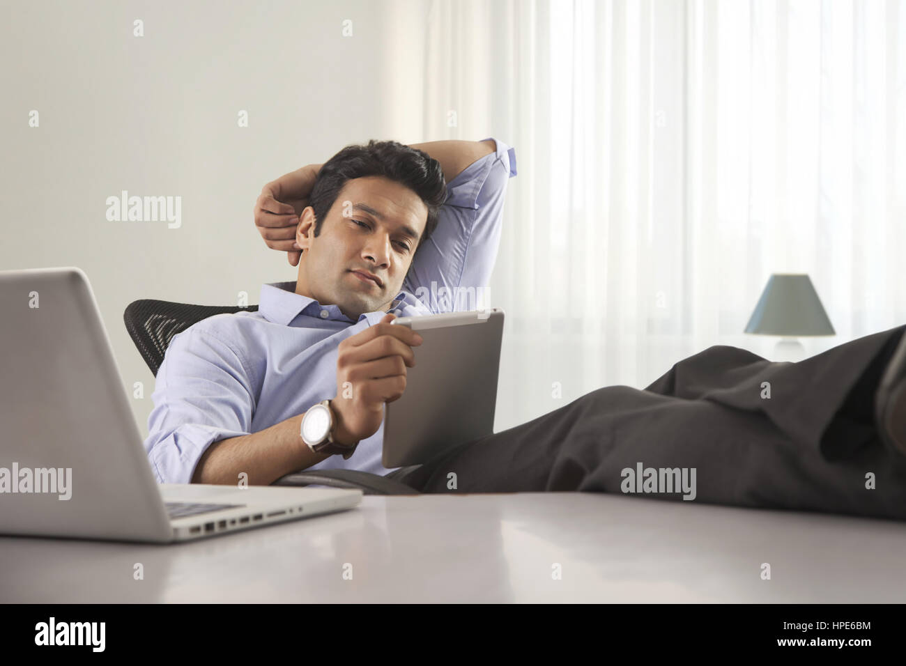 Porträt eines Geschäftsmannes am Schreibtisch mit seinen Füßen bis und mit digital-Tablette Stockfoto