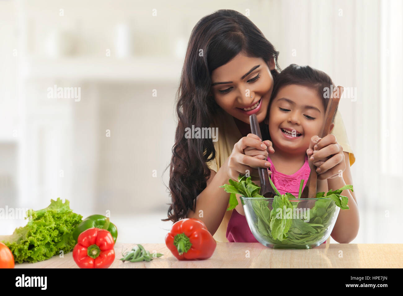 Lächelnde Mutter und Tochter machen Salat für das Mittagessen in der Küche Stockfoto