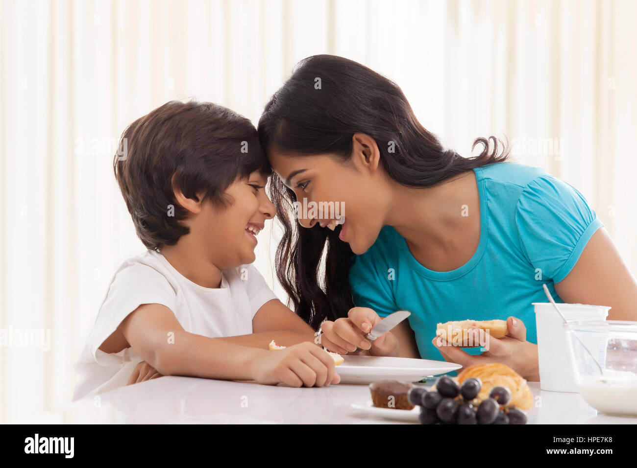 Junge Mutter und ihr Sohn lächelnd mit Köpfen zusammen am Frühstückstisch Stockfoto