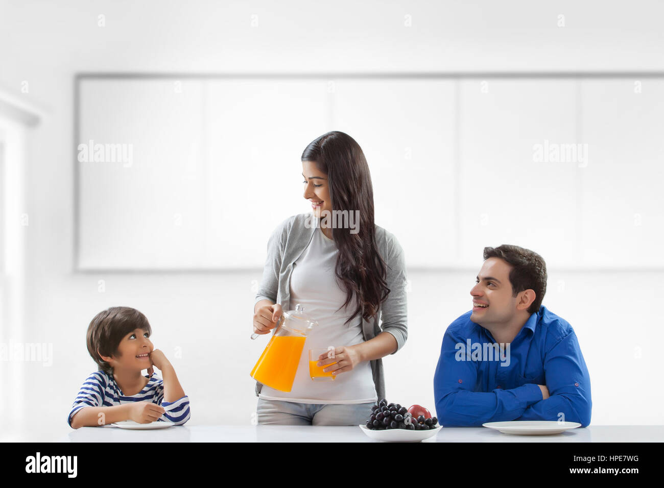 Mutter Gießen Orangensaft für Mann und Sohn in der Küche sitzen Stockfoto
