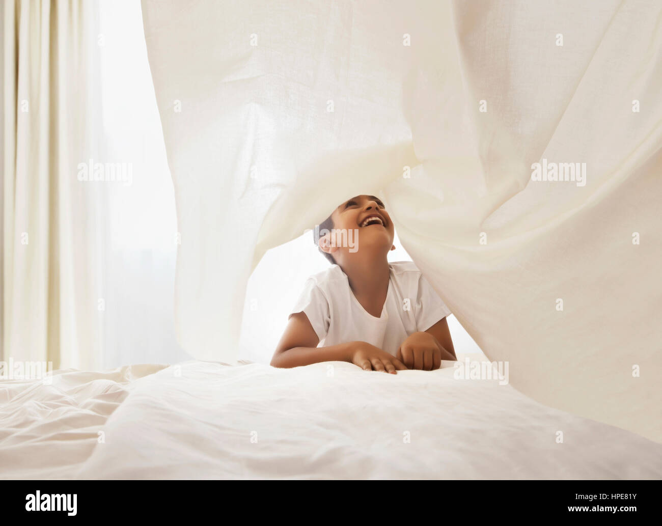 Kleiner Junge spielt unter weißen Bettlaken im Schlafzimmer Stockfoto