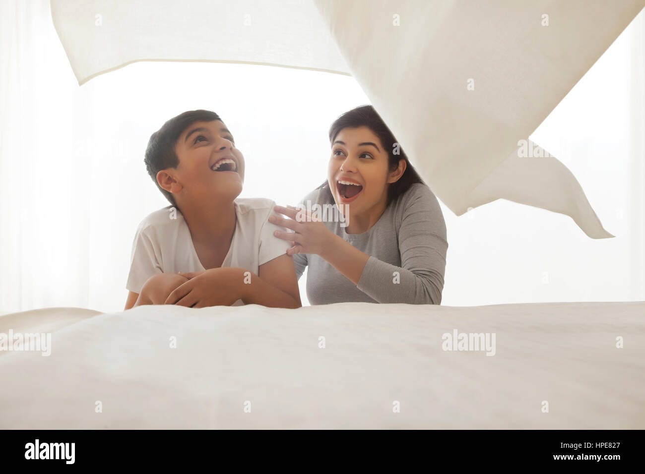 Mutter und Sohn spielt unter weißen Bettlaken im Schlafzimmer Stockfoto