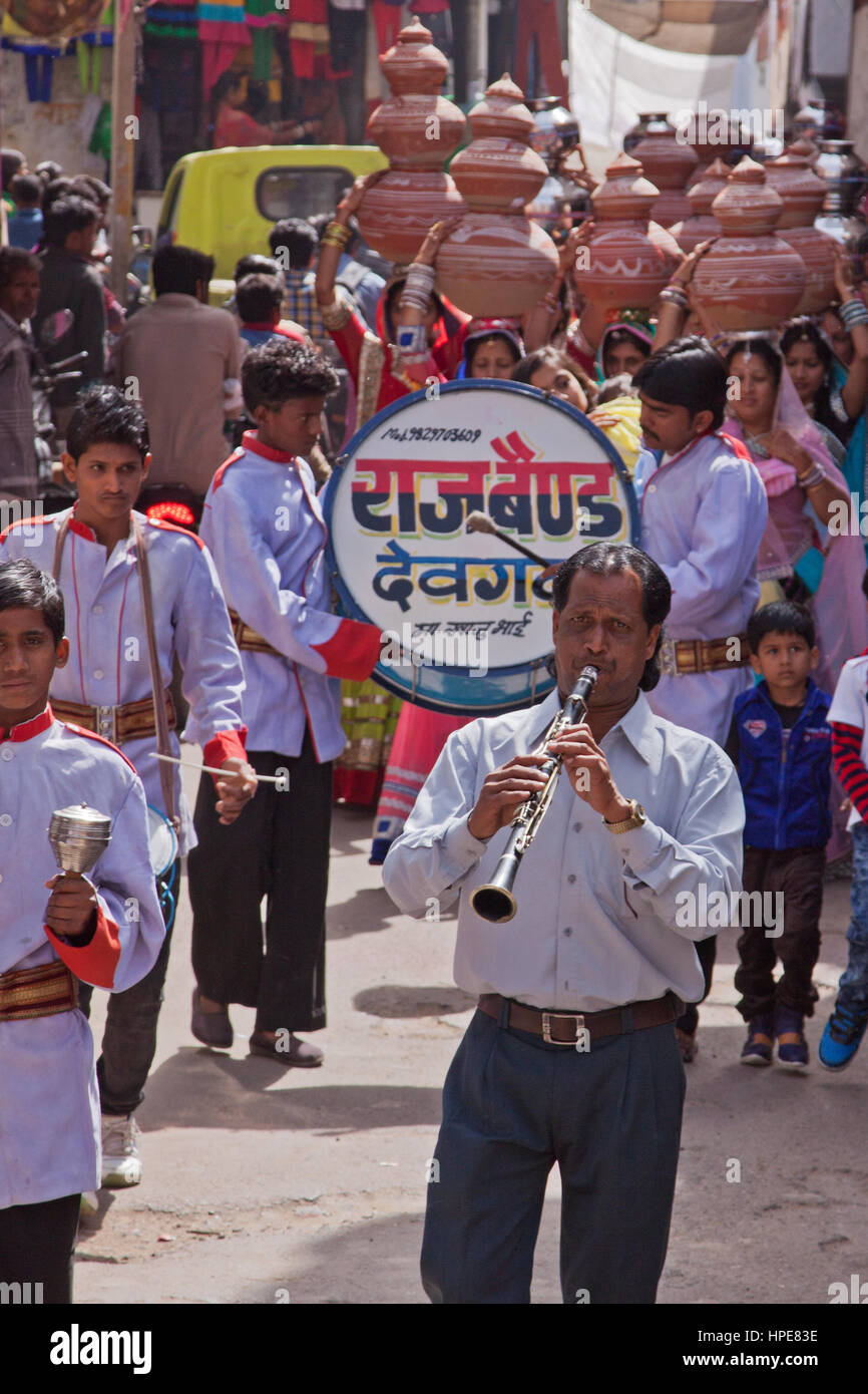 Eine Band, führt eine weibliche Hochzeit Prozession durch die Straßen von Deogarh, Indien. Die Frauen, die nach hinten tragen symbolische Geschirr auf dem Kopf Stockfoto