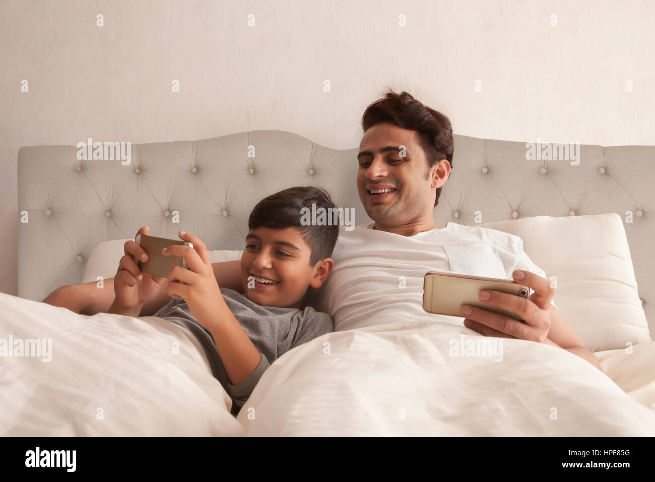 Glücklicher Vater Sohn spielen auf Smartphone im Bett zu betrachten Stockfoto