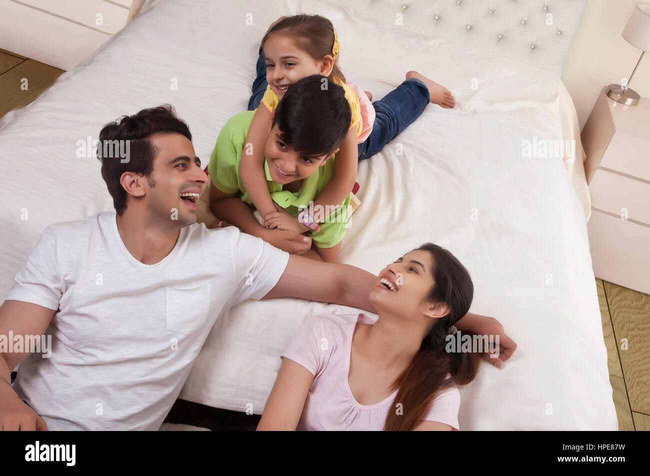 Lächelnd die Eltern an ihre Kinder spielen auf Bett Stockfoto