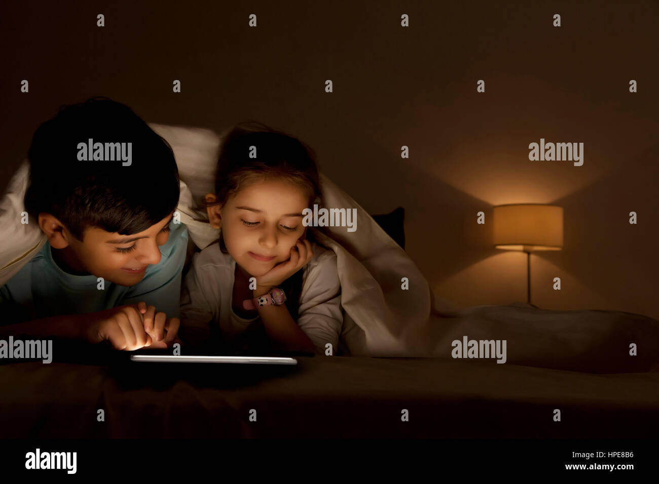 Bruder und Schwester teilen digital-Tablette unter Decke nachts im Schlafzimmer Stockfoto