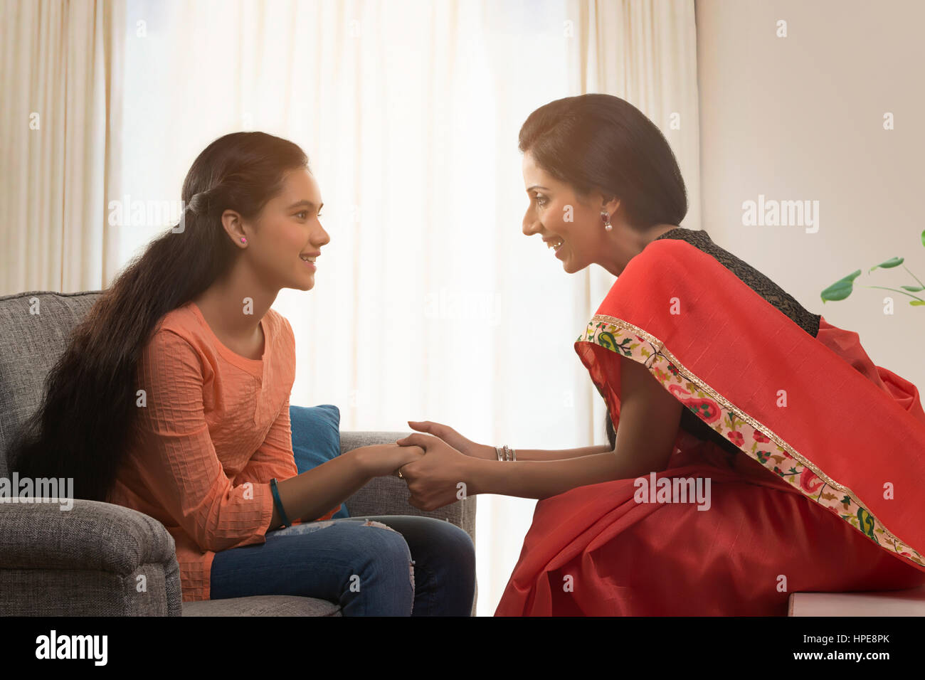 Mutter in einem roten Sari im Gespräch mit ihrer Tochter im Wohnzimmer Stockfoto
