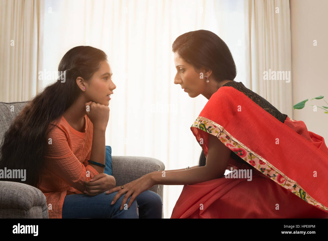 Mutter in einem roten Sari im Gespräch mit ihrer Tochter im Teenageralter im Wohnzimmer Stockfoto