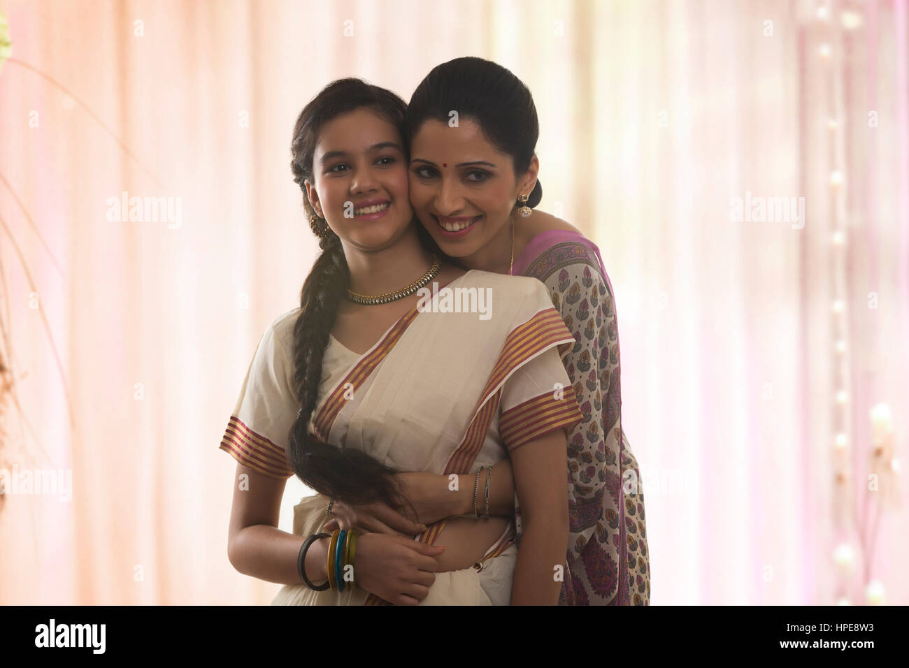 Indische lächelnde Mutter umarmt ihre Tochter von hinten Stockfoto