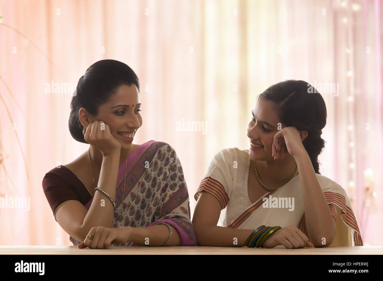 Lächelnde Tochter in Sari und Mutter sitzend mit hand am Kinn Stockfoto