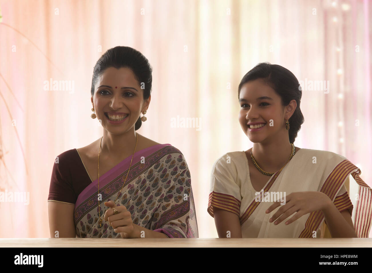 Lächelnde Tochter in Sari und ihre Mutter am Tisch sitzen Stockfoto