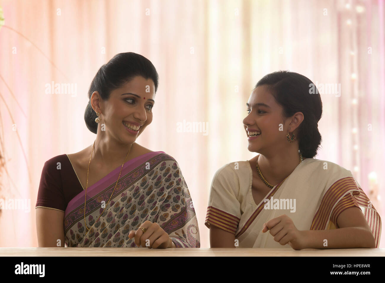 Lächelnd in Sari Tochter mit ihrer Mutter am Tisch sitzen Stockfoto