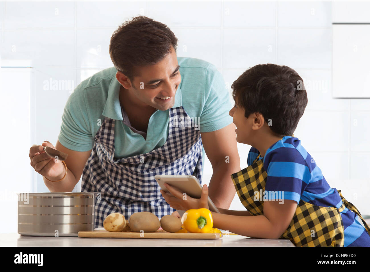 Vater und Sohn in Küche tragen Schürzen Blick auf digital-Tablette Stockfoto